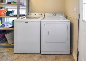 Een wasserette met een voorlader wasmachine en droger, een plank met schoonmaakmiddelen en een betegelde vloer.