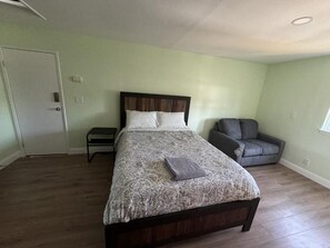Een slaapkamer met een bed, een stoel en een klein tafeltje.