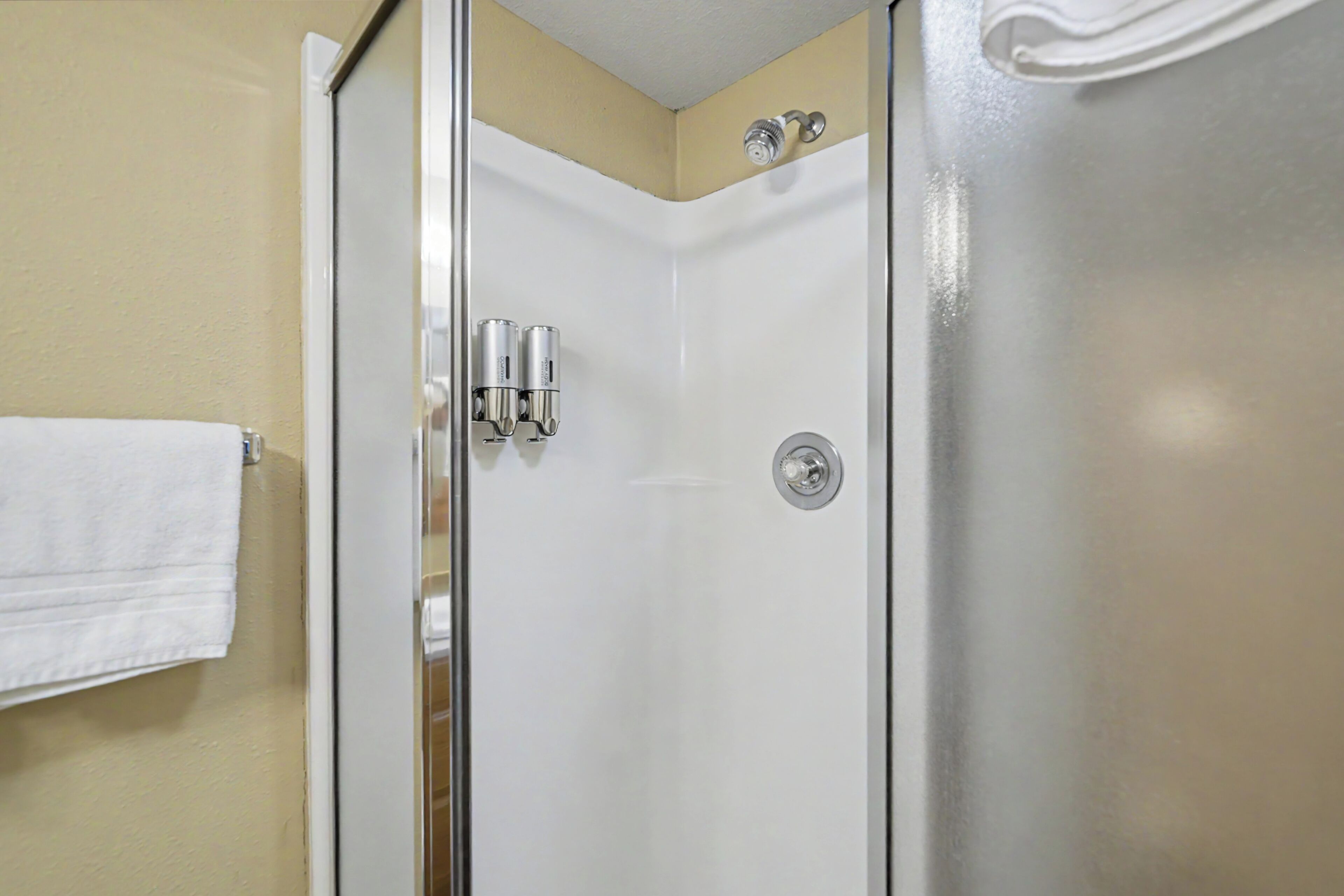 A bathroom with a glass shower door, a white towel hanging on the wall, and a toilet.