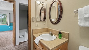 Un baño con lavamanos, espejo, toallero y vistas a una habitación con ventana y cortinas.
