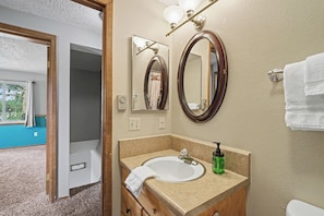 Un baño con lavamanos, espejo, toallero y vistas a una habitación con ventana y cortinas.