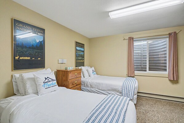 A hotel room with two beds, a dresser, a window with curtains, and two posters of Yellowstone National Park. - Trapper 1 (West Yellowstone)