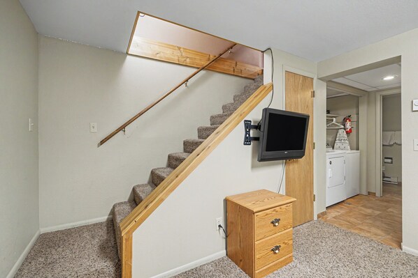 A staircase with a wooden handrail and carpeted steps leading to a landing with a flat-screen TV mounted on the wall. - Trapper 1 (West Yellowstone)