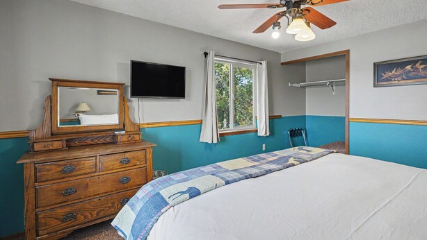 A bedroom with a bed, dresser, television, window, and ceiling fan. - Trapper 1 (West Yellowstone)