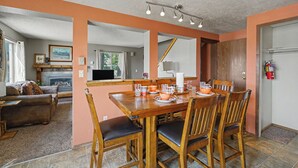 A dining area with a wooden table and chairs, a fireplace, and a view of the living room. - Trapper 1 (West Yellowstone)
