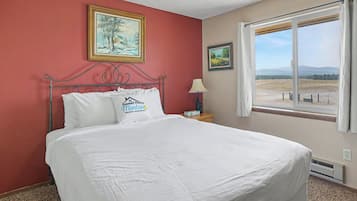 Habitación de hotel con una cama grande, dos cuadros en la pared, un ventanal con vistas y una señal en la almohada.