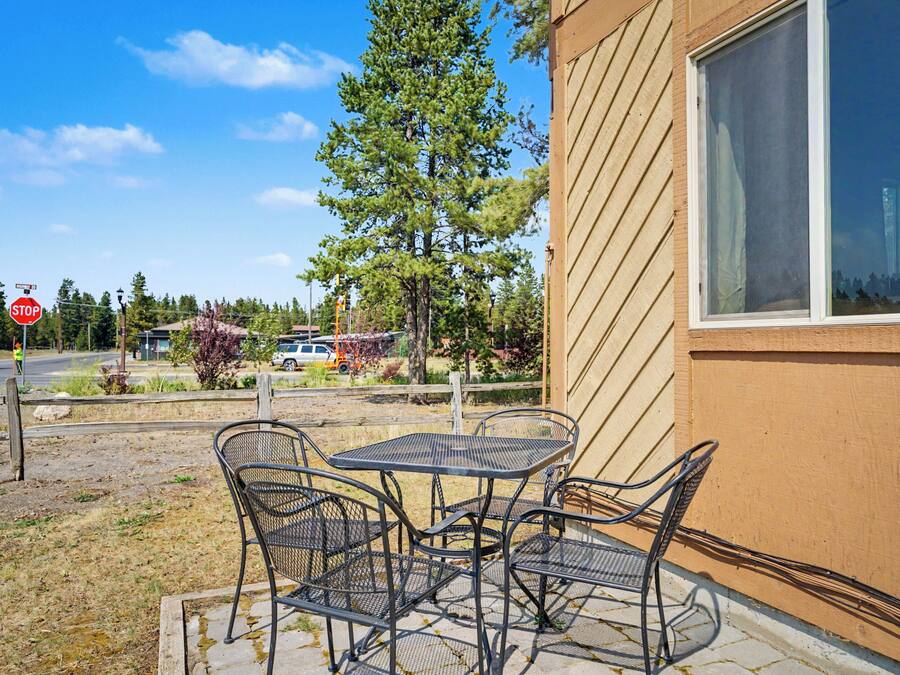 Un patio con sillas y una mesa de metal, una señal de stop y un edificio con una ventana.