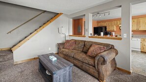 A living room with a brown leather sofa, a wooden coffee table, and a staircase leading to an upper level. - Trapper 1 (West Yellowstone)