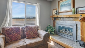 A living room with a sofa, a fireplace, and a window with curtains. - Trapper 1 (West Yellowstone)