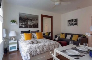 Ein modernes Schlafzimmer mit Bett, Nachttisch und einem Beistelltisch. Es gibt ein Sofa und einen Esstisch mit Stühlen.