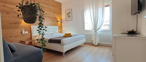 A modern bedroom with a wooden wall, a bed with a white headboard, a bedside table, a hanging plant, and a window with curtains.