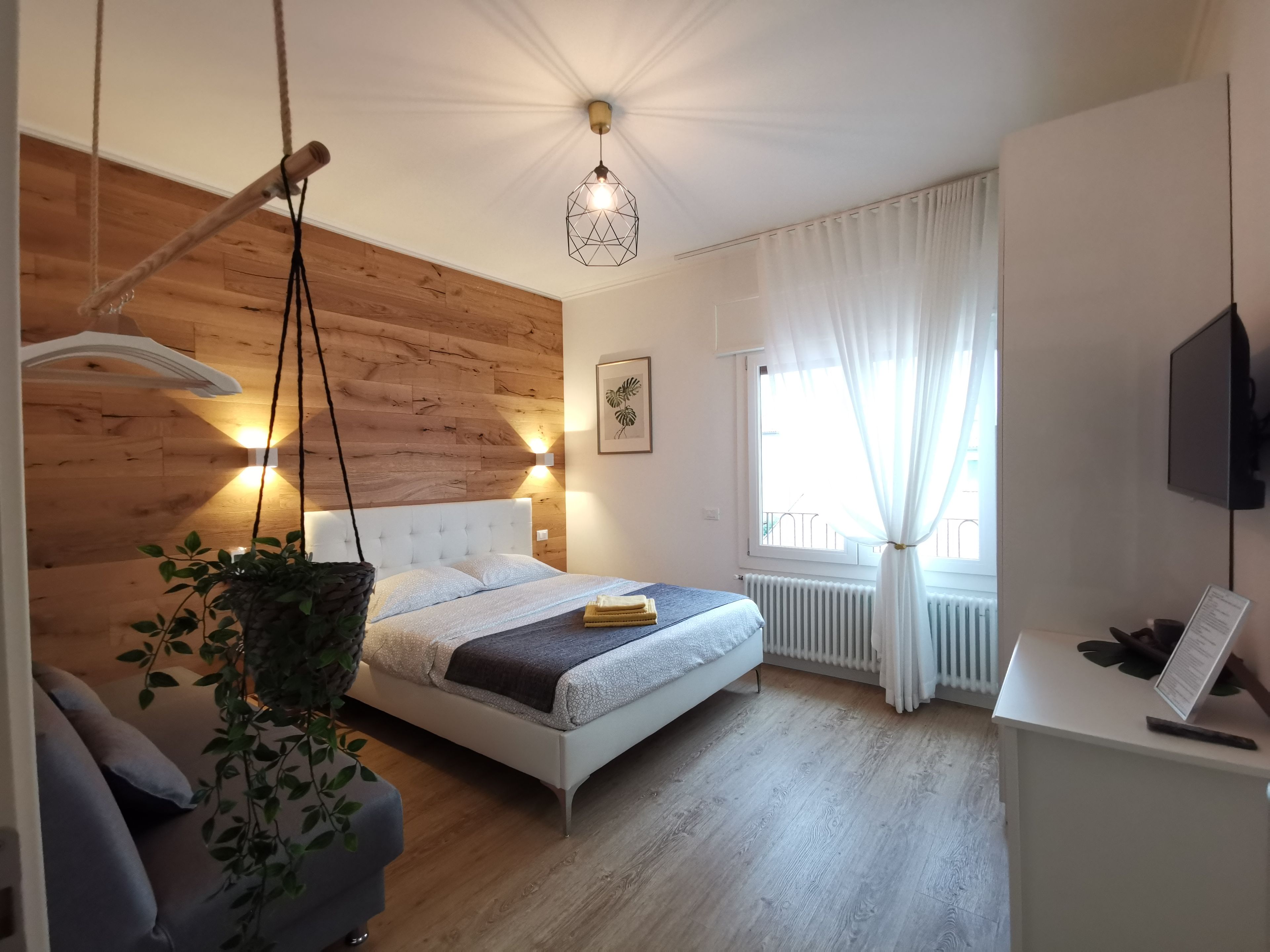 A modern bedroom with a bed, bedside table, hanging plant, and a window with curtains.