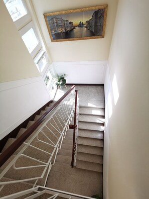 A staircase with a handrail, carpeted steps, and a wall-mounted painting of a cityscape. - KAIXIN'S HOUSE (Private garden + 15-minute bus ride to Venice) (Venezia)