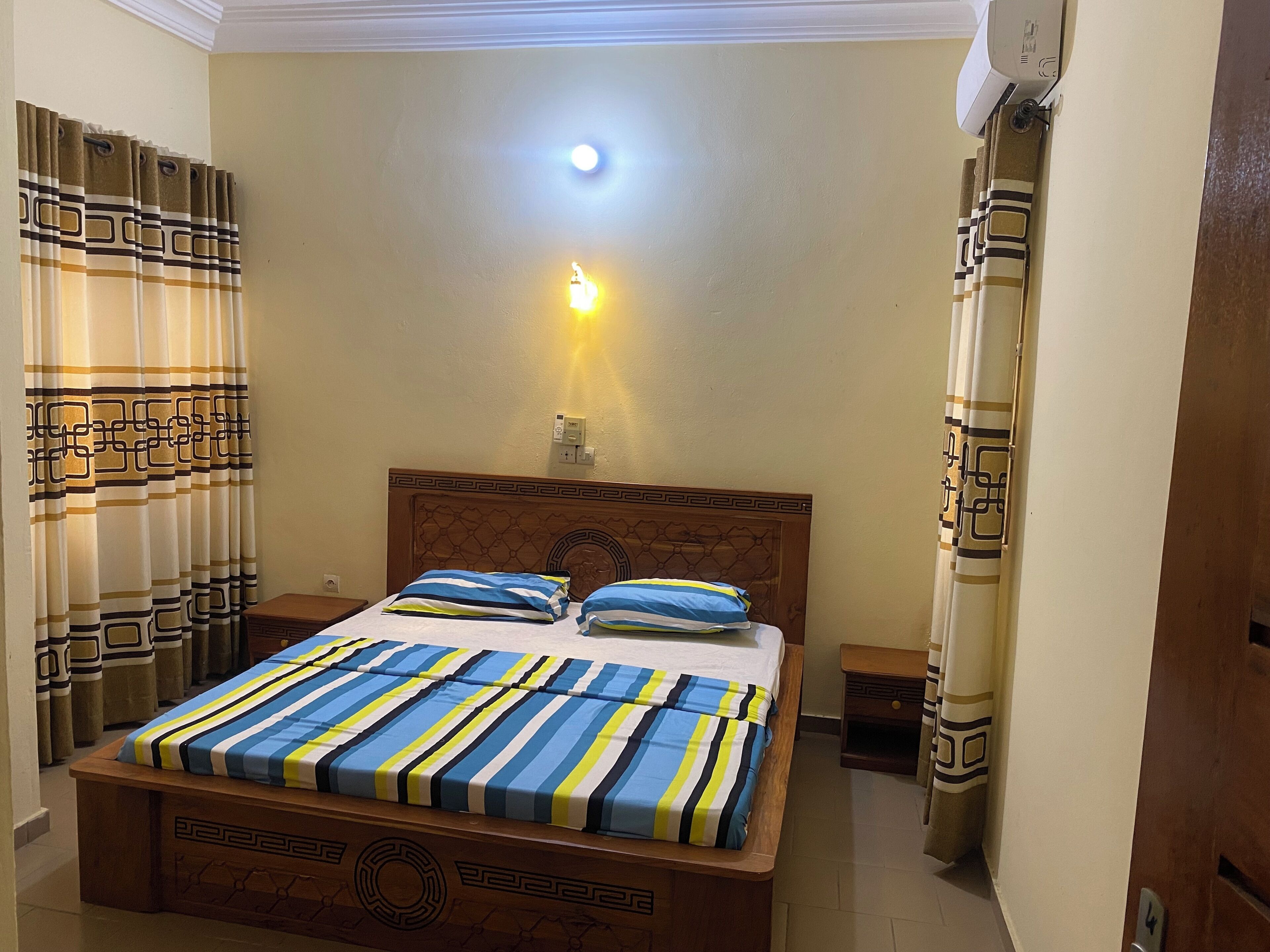 A hotel room with a bed, nightstands, a wall-mounted light, and curtains.