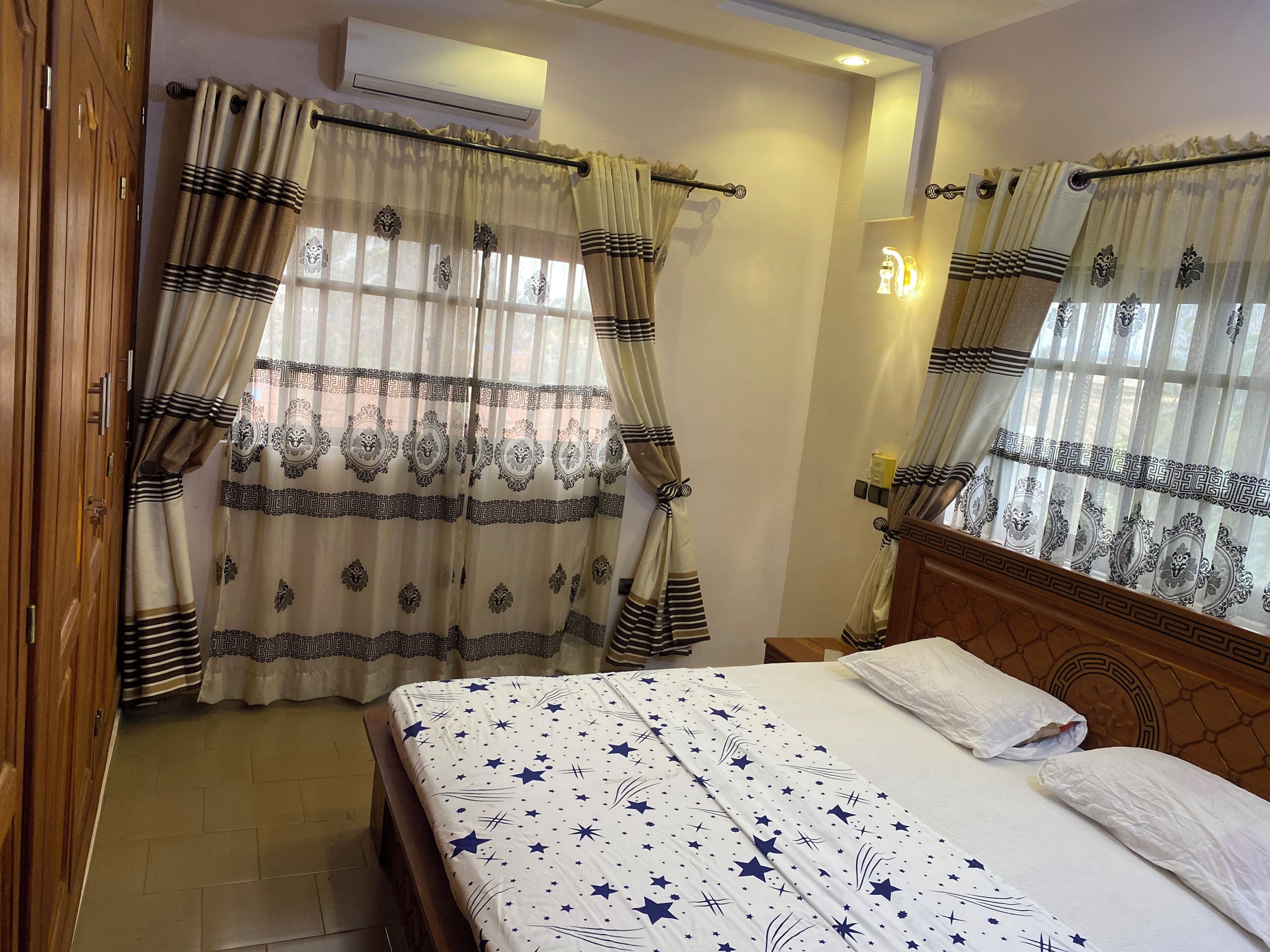 Una habitación de hotel con cama, cortinas, aire acondicionado y mesita de noche.