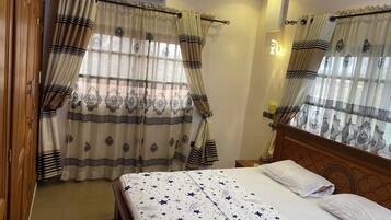 Una habitación de hotel con cama, cortinas, aire acondicionado y mesita de noche.