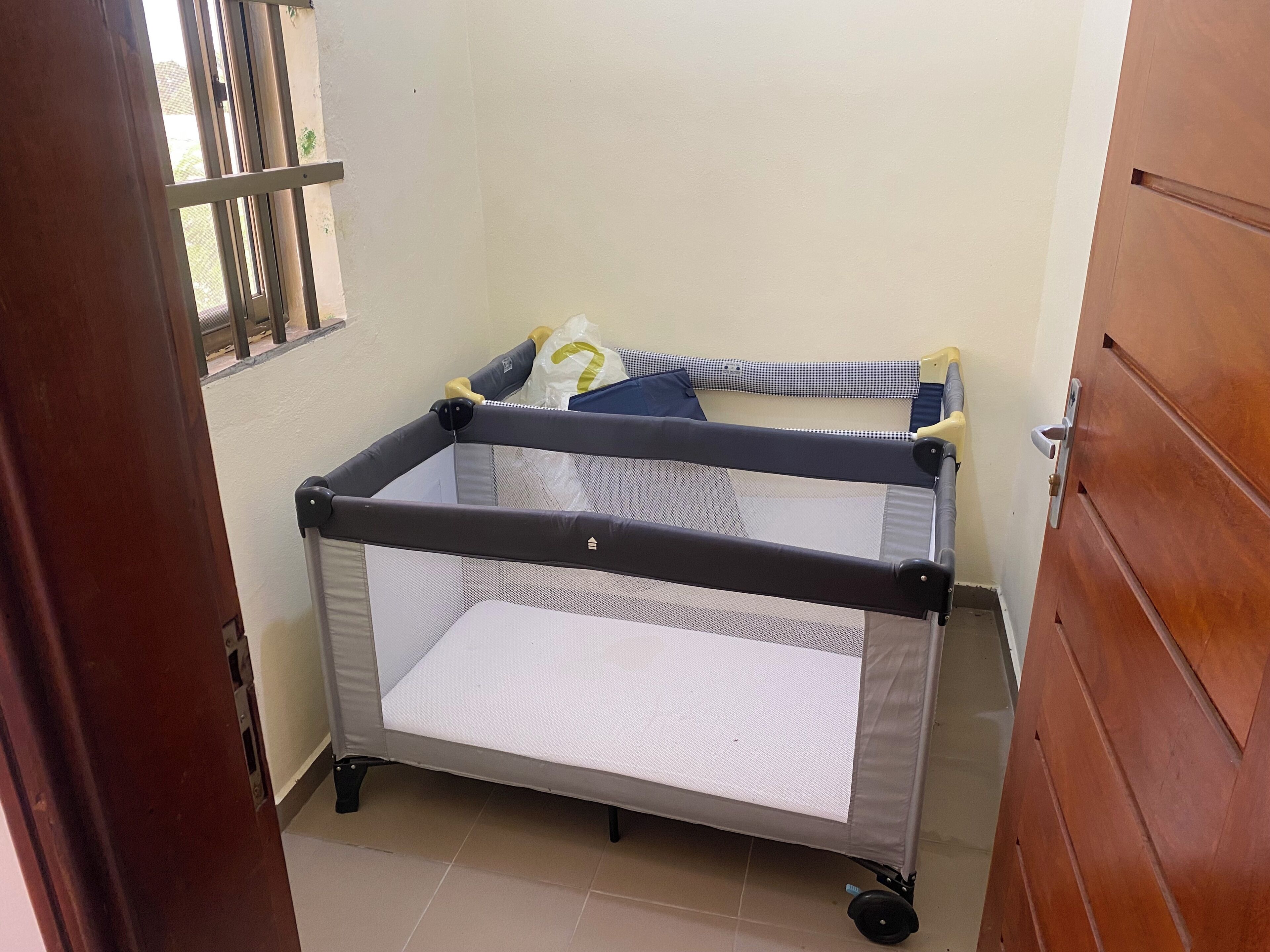 Habitación con cuna portátil, ventana y puerta de madera.