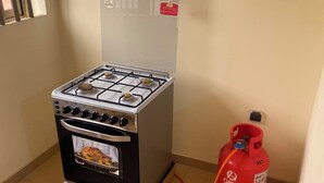A gas stove with four burners and a built-in oven, a red gas cylinder, and a window with blinds. - Seemingly luxurious & peaceful (Godomey)