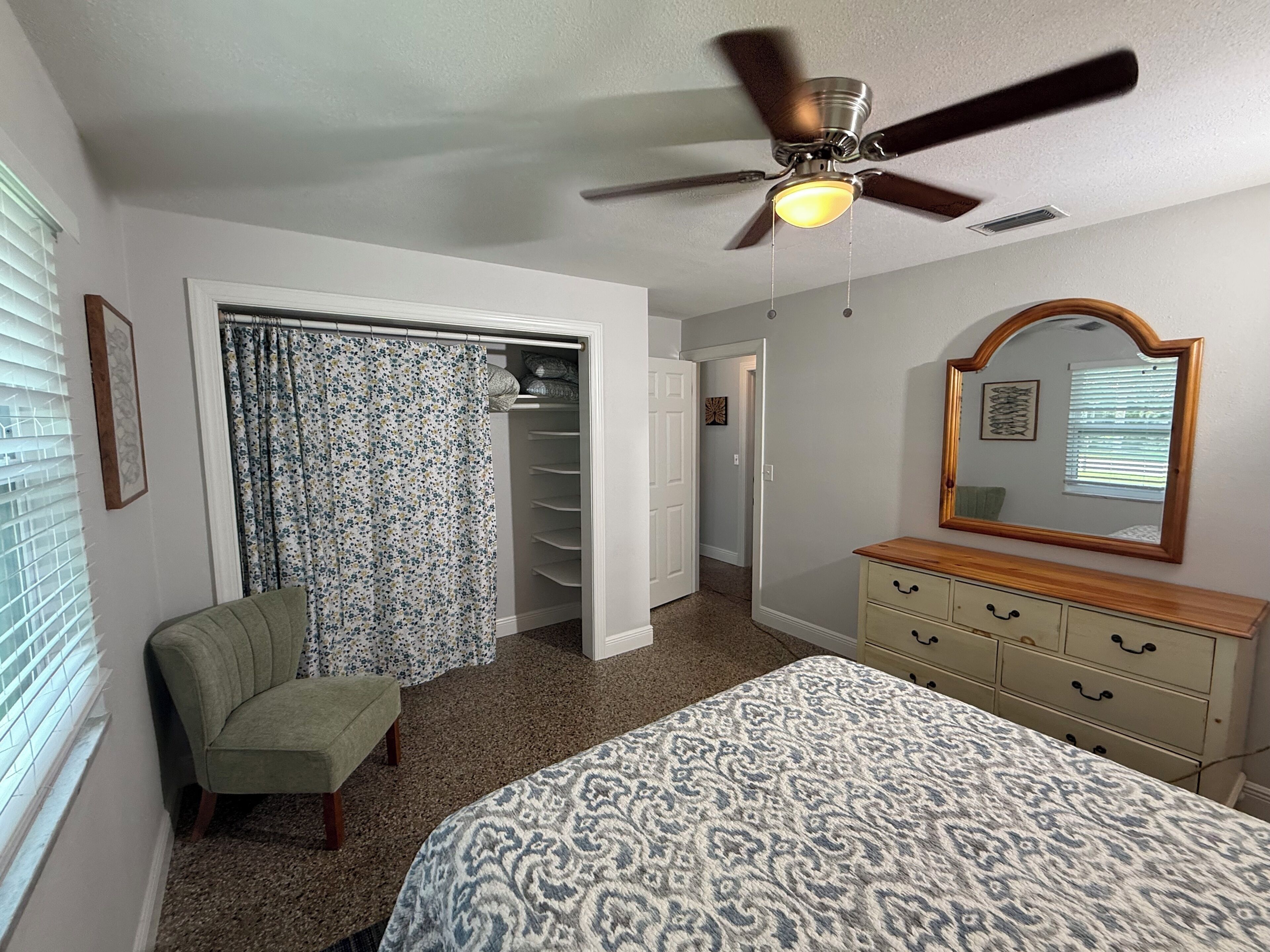 A bedroom with a bed, a chair, a dresser, a ceiling fan, and a walk-in closet.