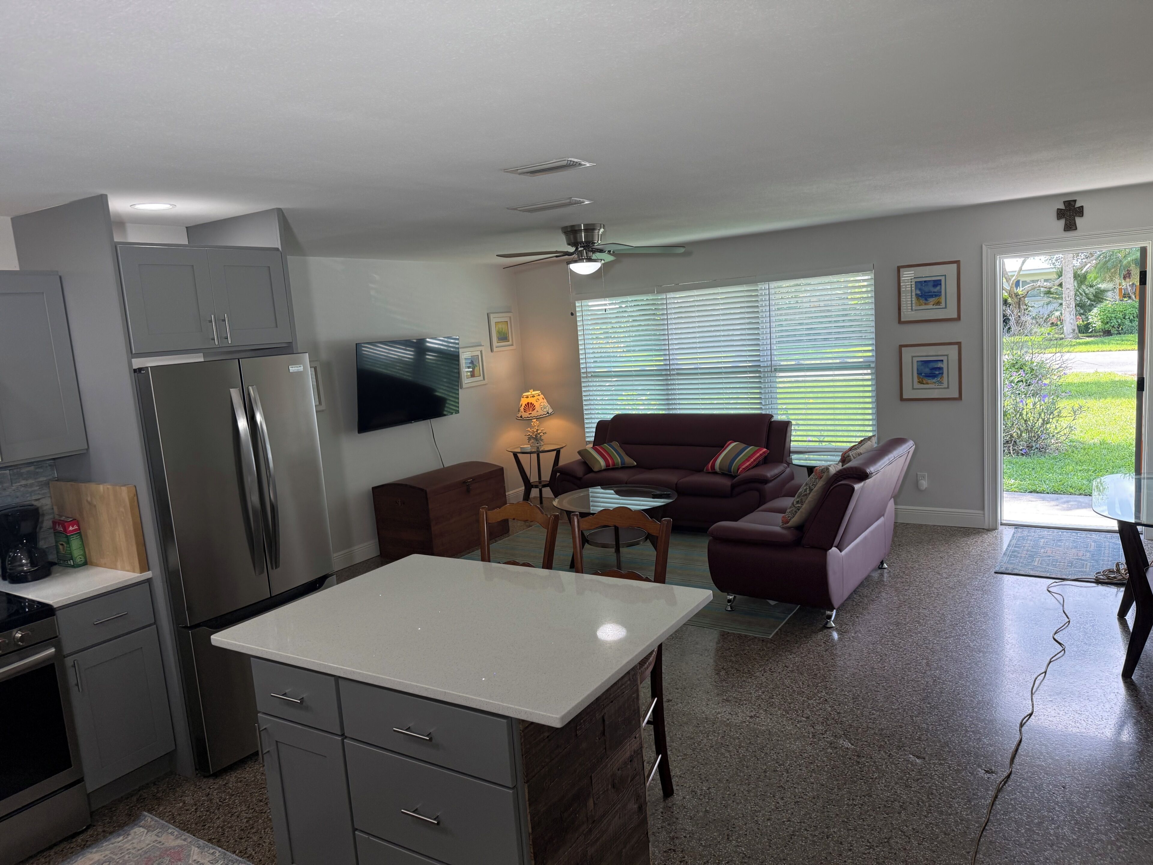 A modern kitchen with a refrigerator, stove, and dining area. There is a living room with a sofa and a television.