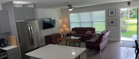 Eine moderne Küche mit Kühlschrank, Herd und Essbereich. Ein Wohnzimmer mit Sofa und Fernseher ist ebenfalls vorhanden.