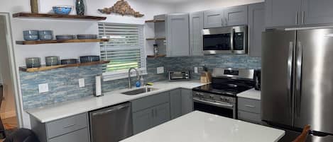 A modern kitchen with grey cabinets, stainless steel appliances, a white countertop, and a window with blinds.