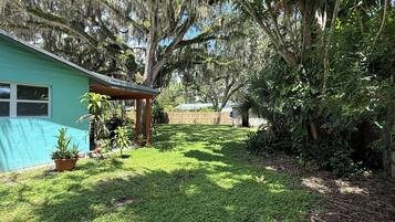 A backyard with a house, a wooden pergola, and a variety of plants.