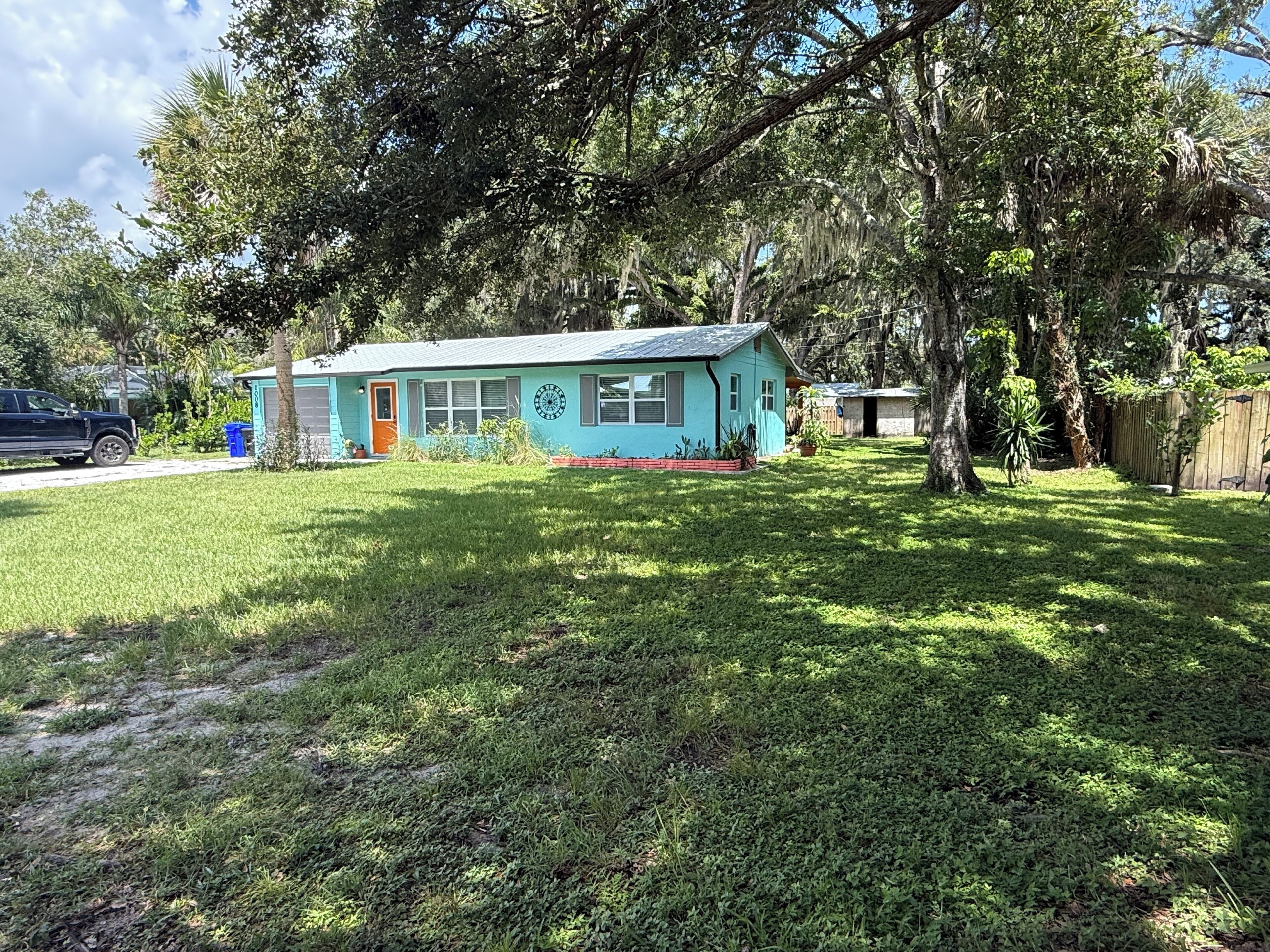 A small house with a blue exterior, a front porch, and a yard with grass and trees.