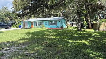 A small house with a blue exterior, a front porch, and a yard with grass and trees.
