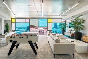 Una sala de estar moderna con una mesa de fútbol de mesa, un sofá y un ventanal con vistas a la ciudad.