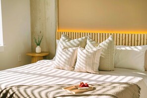 A bed with striped bedding, a wooden headboard, and a bedside table with a plant. - The Emma - Luxury 1BR Condo King Bed, Pool, Gym (Orlando)