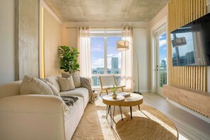 Una sala de estar moderna con un sofá, una mesa de centro, una planta y vistas de la ciudad a través de ventanas amplias.