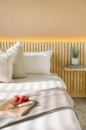 Una cama bien hecha con almohadas y una mesita de noche con un libro y una planta.