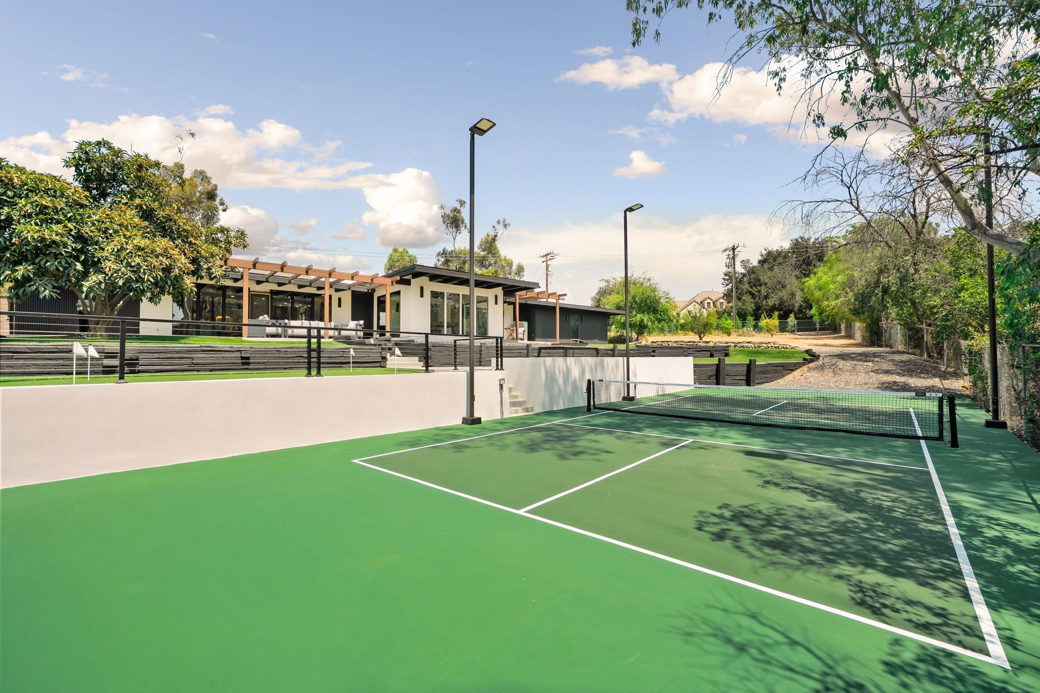 A tennis court with a net, surrounded by a fence, and a building in the background.