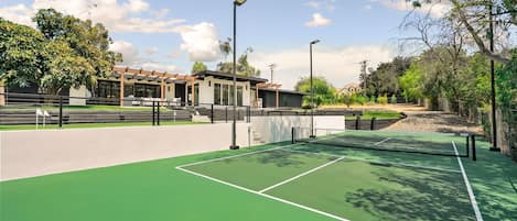 Un court de tennis avec un filet, entouré d’une clôture, et un bâtiment en arrière-plan.