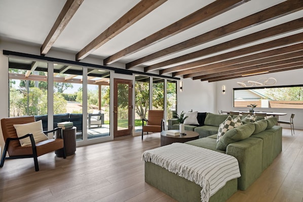 Un amplio salón con un sofá verde, una mesa de centro de madera y vistas al exterior a través de puertas de cristal grandes.