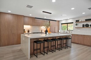 Una cocina moderna con una isla grande, taburetes de bar, armarios de madera y un ventanal con vistas.