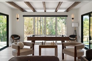 Un interior moderno con una mesa de ajedrez, dos sillas y ventanas amplias con vistas a árboles.