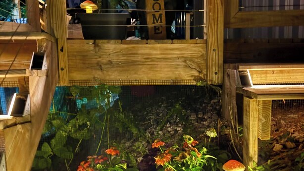 En trækonstruktion med et 'WELCOME'-skilt, et lille bassin med planter og blomster, samt en svampedekoration.