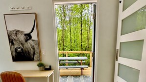 Et værelse med et skrivebord, stol og et stort vindue, der fører ud til en balkon med bænk.