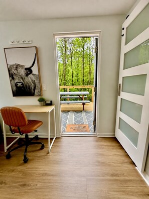 Ein Zimmer mit Schreibtisch, Stuhl und einem großen Fenster zum Balkon mit einer Sitzbank.