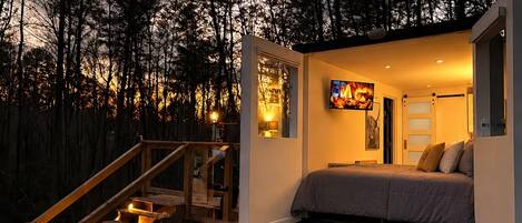A modern bedroom with a bed, a TV, and a staircase leading to an outdoor area.