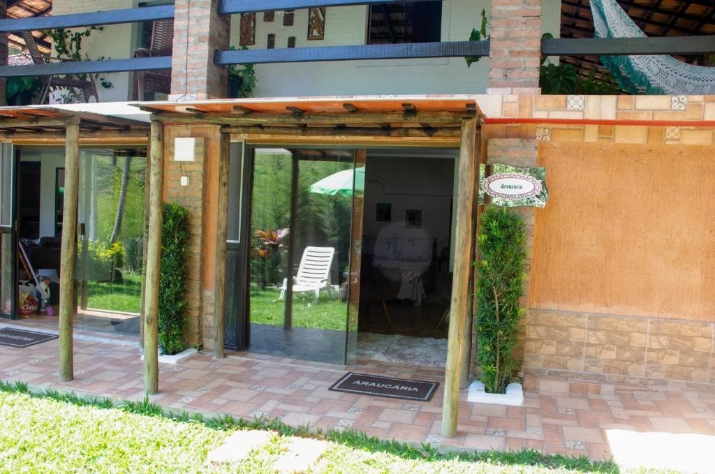 A hotel entrance with a glass door, a sign indicating 'Arauçaria,' and a small garden area with a bench and potted plants.