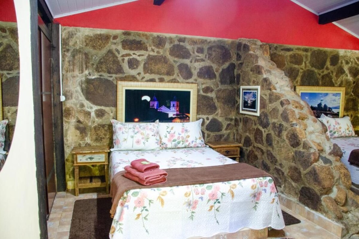 Un dormitori amb una paret de pedra, un llit amb roba de llit floral, una tauleta de nit i una imatge d'un paisatge urbà.