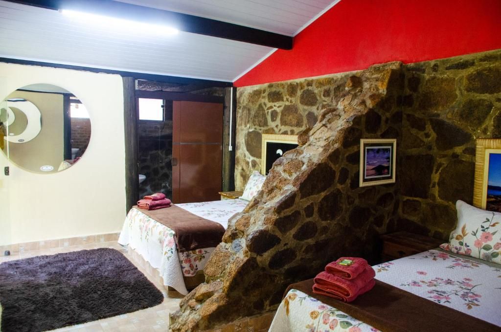 Quarto com duas camas, parede de pedra, espelho e porta para o exterior.