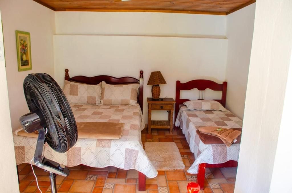 A bedroom with two beds, a standing fan, a nightstand, and a lamp.
