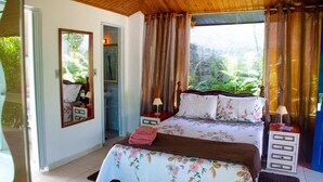 A bedroom with a bed, a mirror, a nightstand, a window with curtains, and a view of greenery outside. - Pousada Estância Vip (Cunha)