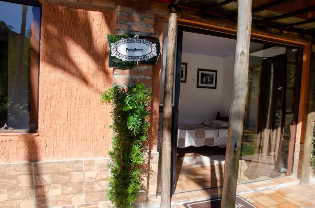 Entrada de um edifício com uma placa indicando 'Paraibuna', uma cama pequena com cobertura branca e uma porta de vidro que dá acesso ao interior.