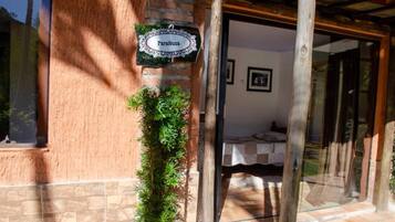 Entrada de um edifício com uma placa indicando 'Paraibuna', uma cama pequena com cobertura branca e uma porta de vidro que dá acesso ao interior.