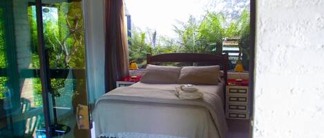 A bedroom with a bed, bedside tables, and a view of greenery outside.